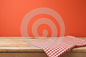 Empty wooden table with red checked tablecloth over red wall background