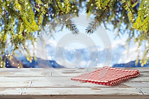 Empty wooden table with red checked tablecloth over winter landscape background.  Christmas and New Year mock up for design and