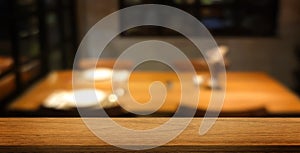 empty wooden table space at foreground with blurred restaurant (cafe) table and tablewares at background.