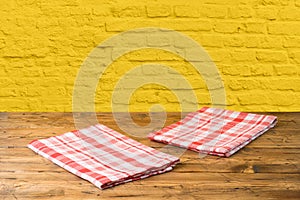 Empty wooden table with tablecloth over yellow brick wall background