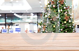 Empty wooden table top over Defocused of decorated Christmas tree with toys, gift box, lights, bauble inside the office building.