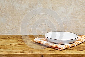 Empty wooden table with white plate above tablecloth over grunge background