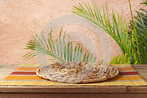 Empty wooden table with wicker place mat over wall with palm tree background. Summer picnic mock up for design and product display