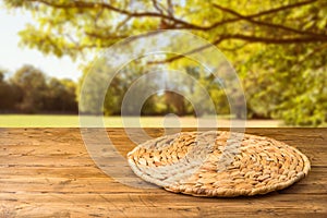 Empty wooden table with wicker round placemat over autumn nature park background