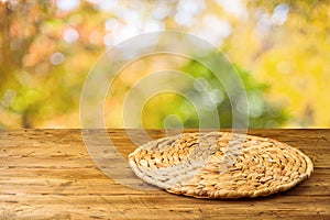 Empty wooden table with wicker round placemat over autumn nature park background