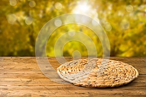 Empty wooden table with wicker round placemat over autumn nature park background