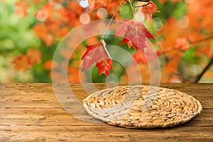 Empty wooden table with wicker round placemat over autumn nature park background