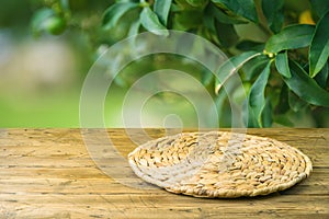 Empty wooden table with wicker round placemat over green garden blurred background. Spring mock up for design