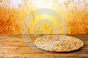 Empty wooden table with wicker round placemat over wheat field background. Harvest mock up background