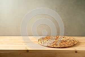 Empty wooden table with wicker round tray over rustic wall background