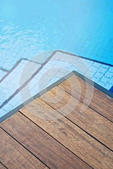 Empty wooden tabletop in front of a swimming pool with blue tile stairs. Concept for product presentation display with summer