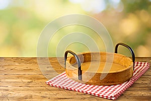 Empty wooden tray with red checked tablecloth on wooden table over autumn bokeh background