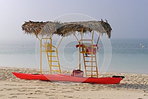 Empty yellow lifeguard towers with palm thatch roof and bright red kayak on a foggy day at deserted beach