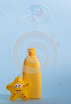 Empty yellow plastic bottle with soap or shampoo on a light blue background with flying soap bubbles..