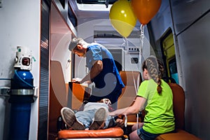 EMT in a blue uniform searching for some supplies in a medical kit, a young woman lyng on a stretcher with an oxygen