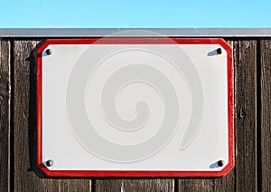 enamel, metal or pottery sign on a rustic wooden wall. red frame, under a bright turquoise sky.