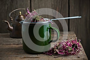 Enameled cup of healthy echinacea tea with tea infuser, dry coneflowers and vintage teapot.