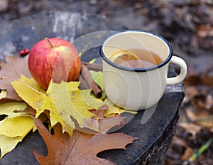 An enameled cup of hot tea, autumn leaves, a rebright autumn portrait of a cute smiling little girl