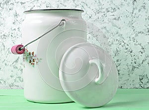 Enameled milk can with lid on white concrete wall background.