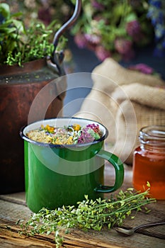 Enameled mug of healing herbs, old tea kettle, honey jar and medical plants.