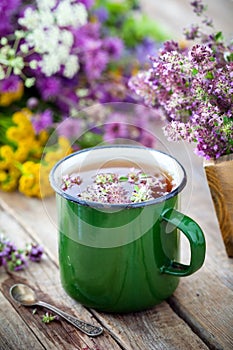 Enameled mug of thyme and medicinal herbs bunch on background.