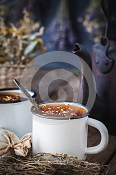 Enameled mugs of healthy herbal tea, tea kettle and healing herbs.