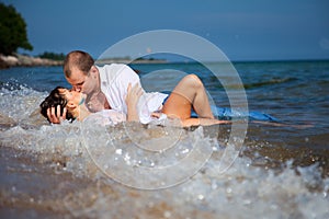 Enamored couple kissing in waves of sandy beach