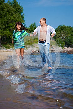 Enamored couple running along the coast of sea