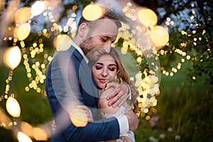 Enamored newlyweds gently embrace. Wedding ceremony in nature. The lights of the electric garland illuminate the wedding