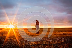 Enchanting sunrise, one male farmer in a field at dawn on the horizon against the backdrop of the rising sun with rays in the