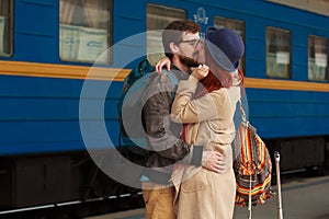 Encounter after a travel of a happy couple hugging in the street in a train station. Beautiful evening warm sunlight