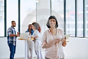 We encourage collaboration in this office. Portrait of a young woman holding a digital tablet in a modern office with