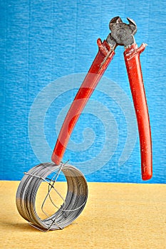 End cutter nipper teetering on steel wire coil, blue backdrop.