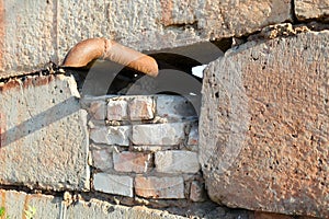The end of an iron pipe sticks out of a concrete brick wall