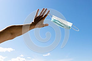 End of quarantine, covid-19. Man taking off and throw away used medical protective mask holds, blue sky background