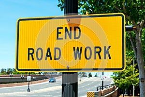 End Road Work traffic sign. Background wide urban street with a few cars