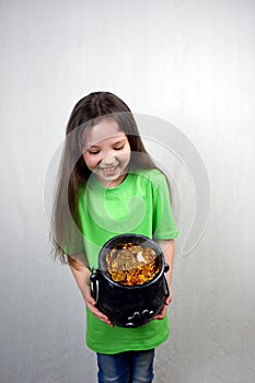 Endearing laughting girl in green T-shirts showing off cast iron pot with four-petal lucky shamrock leaf