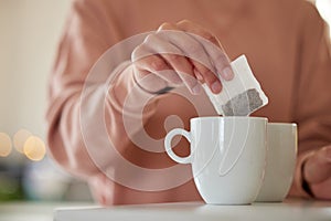 Ending my day with a hot cup of tea. a woman dropping a tea bag into a waiting mug.