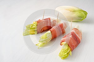 Endive or Chicory rolls with ham, cheese and apple slices, healthy snack on on a white wooden table, copy space