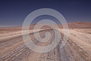 Endless dirt road to infinity of salt flat plateau contrasting with blue cloudless sky.