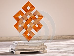 Endless Knot, Buddhist symbol. 3D illustration of the Buddhist symbol - Endless Knot - made of wood on a marble base in a warm lig