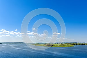 Endless summer landscape. Lake, forest and clear blue sky with beautiful little clouds.