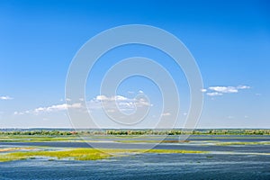 Endless summer landscape. Lake, forest and clear blue sky with beautiful little clouds.