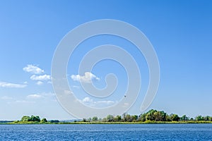 Endless summer landscape. Lake, forest and clear blue sky with beautiful little clouds.