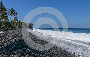 An endless virgin pebble beach with palm trees and tropical vegetation on Bali Island in Indonesia. The waves wash the stony coast