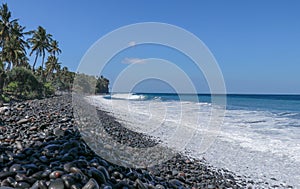 An endless virgin pebble beach with palm trees and tropical vegetation on Bali Island in Indonesia. The waves wash the stony coast