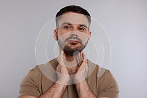 Endocrine system. Man doing thyroid self examination on light grey background