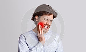 Endure pain. Sad man suffers from pain in his teeth and presses hand to red spot photo