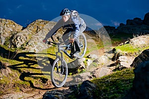 Enduro Cyclist Riding the Bike on the Rocky Trail at Night. Extreme Sport Concept. Space for Text.