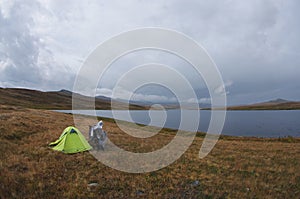 Enduro motorcycle alone traveler near green tent at dark gloom fog steppe shore of lake